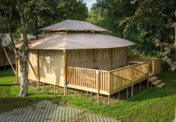 Stardust 40 Family Lodge safari tent with a wooden deck in a lush, wooded campsite, summer setting.