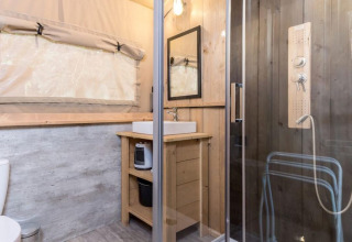 Badezimmer im Safari-Zelt mit Holzdekor, Dusche, Waschbecken und Fenster in Petite Suisse, Belgien.