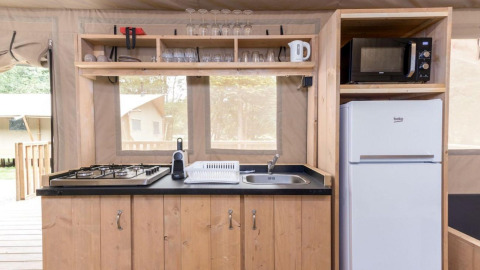 Küchenbereich eines Safarizeltes im Stardust 40 Family Lodge, Petite Suisse, Belgien, mit Herd, Kühlschrank und Mikrowelle.