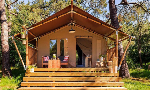 Tienda safari Comet 27 Lodges con terraza de madera y asientos rodeada de vegetación en Petite Suisse, Bélgica.