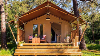 Safari tent Comet 27 Lodges with cozy wooden deck and seating in lush surroundings at Petite Suisse, Belgium.