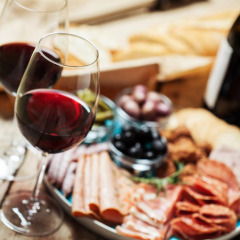 Dos copas de vino tinto y una tabla de embutidos con pan, carnes y aceitunas en un parque de glamping.