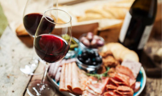 Zwei Gläser Rotwein und eine Wurstplatte mit Brot, Fleisch und Oliven in einem Glamping-Ferienpark.