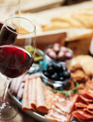 Dos copas de vino tinto y una tabla de embutidos con pan, carnes y aceitunas en un parque de glamping.