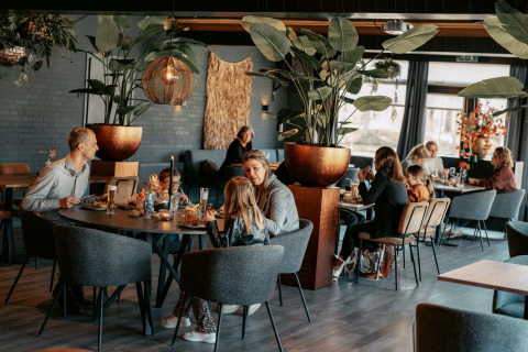 Des clients dînent dans un restaurant moderne avec de grandes plantes au Camping de Italiaanse Meren en Gueldre.