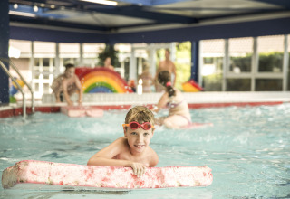 Un niño juega en una piscina cubierta con una tabla flotadora en Holiday Park Mölke, Overijssel, Países Bajos.