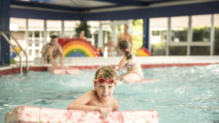 Un niño juega en una piscina cubierta con una tabla flotadora en Holiday Park Mölke, Overijssel, Países Bajos.