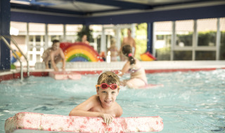 Un niño juega en una piscina cubierta con una tabla flotadora en Holiday Park Mölke, Overijssel, Países Bajos.