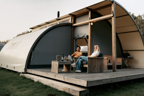 Deux personnes se détendent sur la terrasse d’une tente glamping au Camping de Italiaanse Meren, en Gueldre.