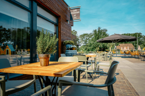 Terraza al aire libre en Camping de Italiaanse Meren con mesas, sillas y clima soleado en Gelderland.