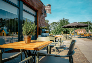 Terrasse extérieure du Camping de Italiaanse Meren avec des tables, des chaises et du soleil à Gelderland.