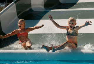 Zwei Kinder in Badesachen rutschen fröhlich eine Wasserrutsche im Camping de Italiaanse Meren in Gelderland hinab.