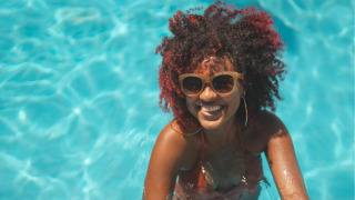 Mujer con gafas de sol sonríe en la piscina de un parque vacacional con alojamiento glamping.