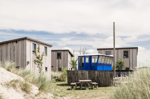 Cabañas de madera y un vagón azul entre dunas en Duynpark Het Zwanenwater, parque vacacional en Holanda del Norte.