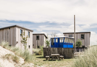 Wooden cabins and a blue wagon among sand dunes at Duynpark Het Zwanenwater holiday park in North-Holland.