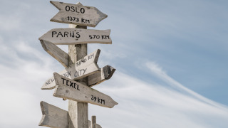 Holzwegweiser mit Entfernungsangaben zu Oslo, Paris, New York City und Texel im Duynpark Het Zwanenwater.