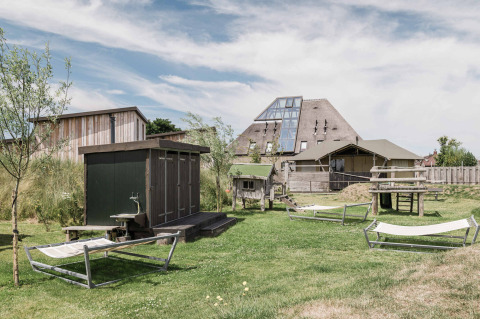 View of Duynpark Het Zwanenwater holiday park with hammocks, wooden sheds, and modern building in North-Holland.