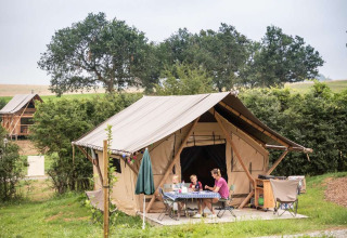Familie campt vor einem Zelt im Huttopia Pays de Cordes sur Ciel in Occitanie, Frankreich.