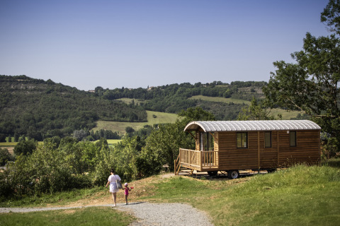 Madre e hijo caminan cerca de una cabaña de madera en Huttopia Pays de Cordes sur Ciel, Occitanie, Francia.