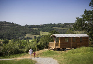 Mor og barn går nær en træhytte med udsigt over bakker i Huttopia Pays de Cordes sur Ciel, Occitanie, Frankrig.