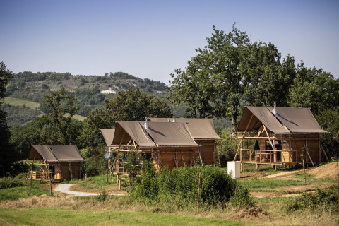 Cabañas glamping en Huttopia Pays de Cordes sur Ciel, Occitania, Francia, rodeadas de paisaje verde.