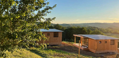 Træhytter i Huttopia Pays de Cordes sur Ciel, omgivet af natur og bakker i Occitanie, Frankrig ved solnedgang.