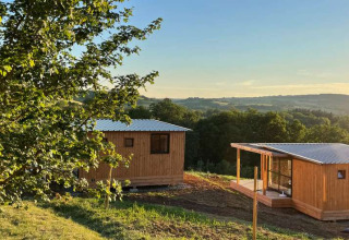 Træhytter i Huttopia Pays de Cordes sur Ciel, omgivet af natur og bakker i Occitanie, Frankrig ved solnedgang.
