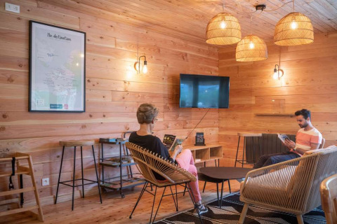 Afslappende loungeområde med trævægge, moderne møbler og mennesker, på Huttopia Pays de Cordes sur Ciel.