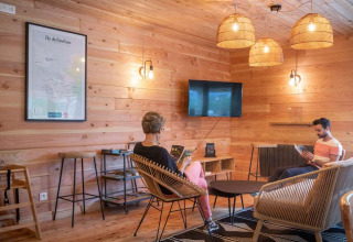 Afslappende loungeområde med trævægge, moderne møbler og mennesker, på Huttopia Pays de Cordes sur Ciel.