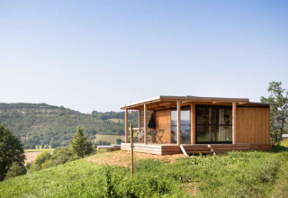 Wooden cabin at Huttopia Pays de Cordes sur Ciel holiday park in Occitanie, France, overlooking green hills.