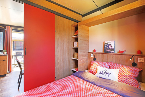Knusse slaapkamer in Chalet Evasion Vista met rode tinten, houtaccenten en natuurlijk licht.