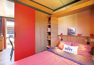 Knusse slaapkamer in Chalet Evasion Vista met rode tinten, houtaccenten en natuurlijk licht.