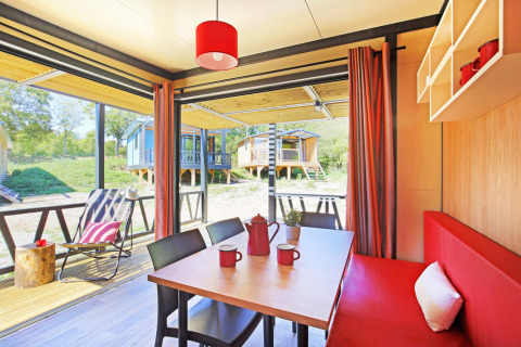 Interieur van Chalet Evasion Vista met rode accenten, eettafel en uitzicht op kleurrijke chalets buiten.
