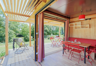 Chalet Evasion Vista: Acogedora cabaña con mesa roja, terraza abierta y vistas a la naturaleza verde.