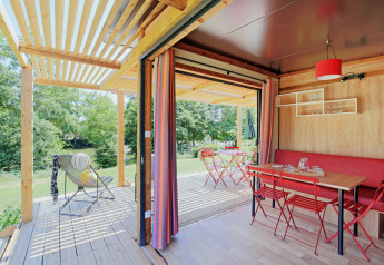 Chalet Evasion Vista: Acogedora cabaña con mesa roja, terraza abierta y vistas a la naturaleza verde.