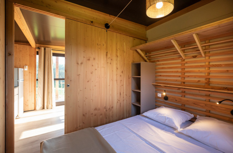 Dormitorio luminoso de madera con cama doble en el Chalet Evasion Vista de Huttopia De Roos, Países Bajos.