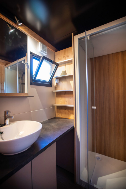 Moderne badkamer in Chalet Evasion Vista met waskom, glazen douche, open raam en houten schappen.