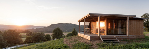 Zonsondergang aan Chalet Evasion Vista, een houten chalet met terras en zicht op glooiende heuvels en natuur.