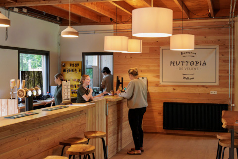 Recepción del Camping Huttopia De Veluwe en Gelderland, Países Bajos, con decoración de madera y personal amable.