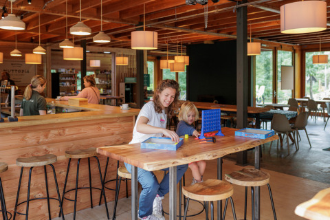 Eine Mutter und ihr Kind spielen ein Brettspiel in der gemütlichen Lounge von Camping Huttopia De Veluwe.