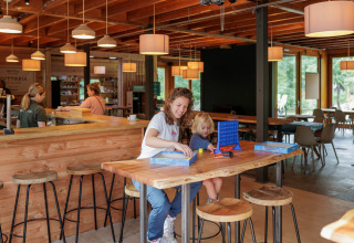 A mother and child enjoy a board game together at a table inside Camping Huttopia De Veluwe in Gelderland.