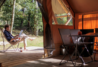 Man ontspant met boek en koffie voor een tent bij Camping Huttopia De Veluwe, Gelderland, Nederland.