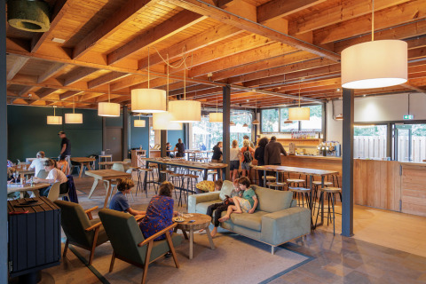 Café interior en Camping Huttopia De Veluwe, Gelderland, Países Bajos, con huéspedes y decoración de madera moderna.