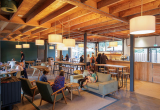 Indoor café area at Camping Huttopia De Veluwe in Gelderland, Netherlands, with guests and modern wood décor.