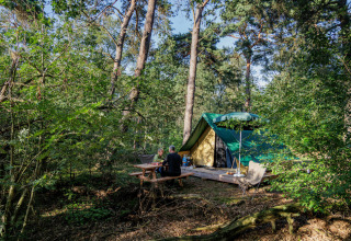 Kampeerders aan picknicktafel en tent in een bos bij Camping Huttopia De Veluwe, Gelderland, Nederland.