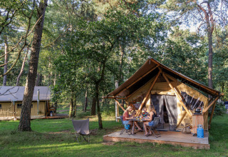 Gezin geniet van een maaltijd voor een tent in het bos bij Camping Huttopia De Veluwe in Gelderland.