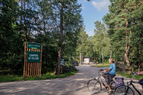 Entrance to Camping Huttopia De Veluwe in Gelderland, Netherlands, with cyclists and surrounding green trees.