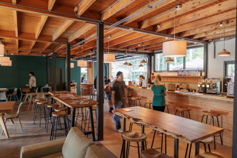 Bright café with wooden décor, exposed beams, and a bar at Camping Huttopia De Veluwe in Gelderland, Netherlands.