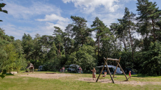 Kinder spielen auf einem Spielplatz im Grünen bei Camping Huttopia De Veluwe, Gelderland, Niederlande.