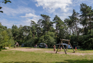 Kinder spielen auf einem Spielplatz im Grünen bei Camping Huttopia De Veluwe, Gelderland, Niederlande.